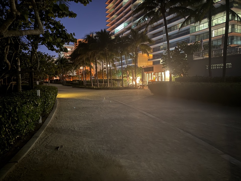 Bal Harbour beachside walkway at twilight with illuminated luxury tower and palm trees
