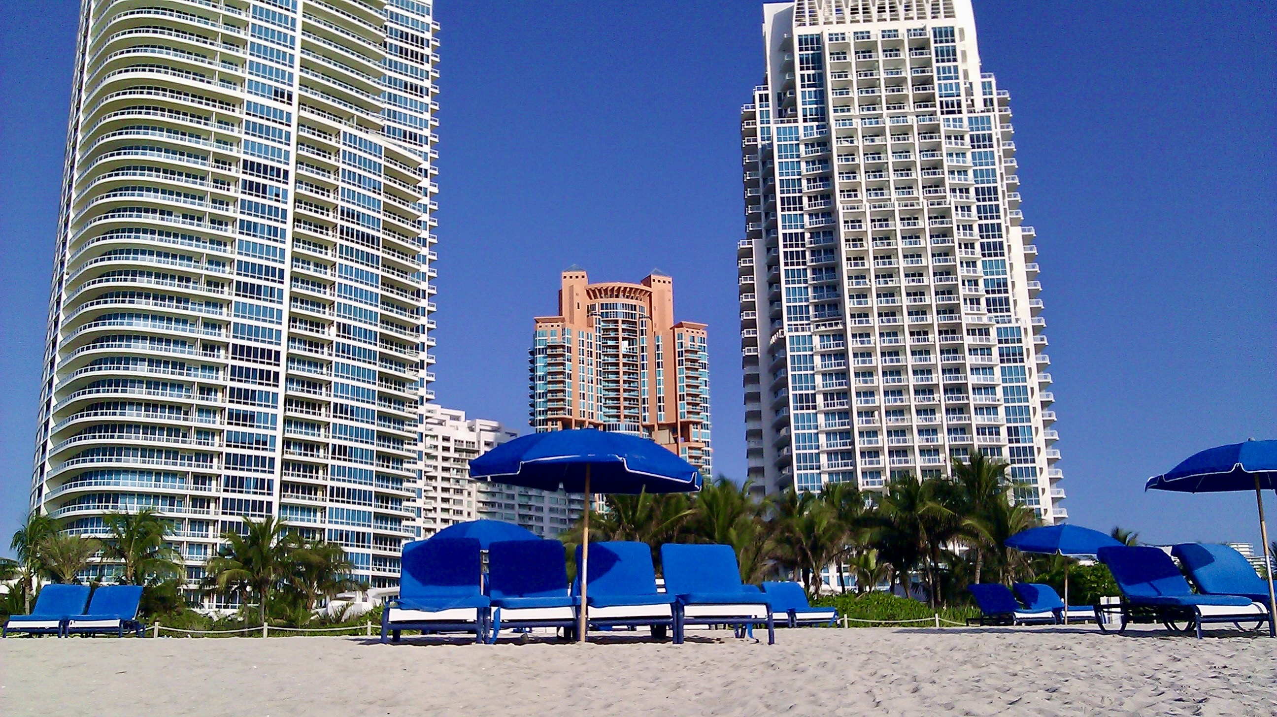 Beachfront luxury condominiums along South of Fifth with blue loungers on the sand and ocean views
